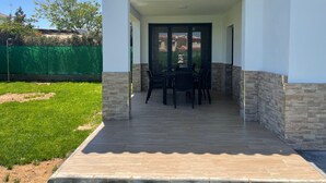 Un patio techado con una mesa y sillas, una valla verde y un cielo despejado.