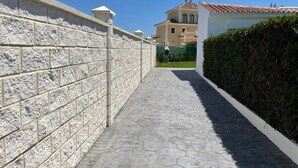 Un sendero pavimentado que conduce a un edificio, con un muro de piedra a un lado y un seto al otro.