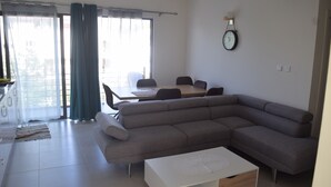 A modern living room with a grey sectional sofa, a white coffee table, and a dining area with a table and chairs.