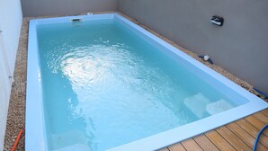 A rectangular swimming pool with a light blue interior, surrounded by a pebble bed and wooden deck flooring.