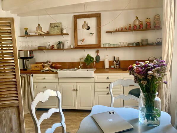 Cozinha com armários brancos, bancada de madeira e área de jantar com um laptop e um vaso de flores.