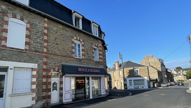 Vista de la calle con una panadería llamada 'BOULANGERIE' a la izquierda, un paso de peatones y coches aparcados.