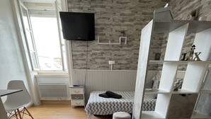 Una habitación moderna con pared de piedra, una cama con cubrecama estampado, radiador blanco, escritorio con silla y televisor montado en la pared.