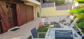 Un patio con mobiliario exterior, una puerta de madera cerrada y una pared amarilla con barandilla blanca.