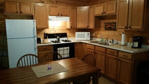 A kitchen with wooden cabinets, a stove, a microwave, and a refrigerator. There is a dining table with chairs.