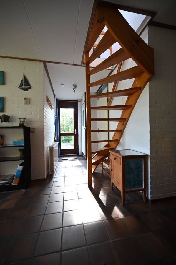 A staircase with a wooden handrail leading to a landing, a tiled floor, and a door leading outside.