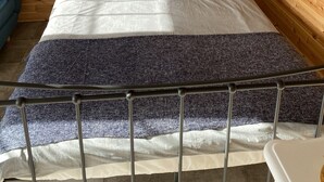 Une pièce aux murs lambrissés, avec un lit, une chaise bleue et une guirlande accrochée au mur.
