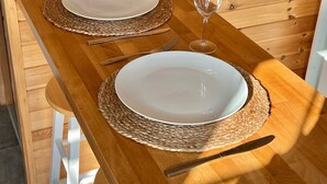 Une table de salle à manger en bois, avec deux assiettes blanches et deux verres à vin, le tout agrémenté de sets de table en fibres tressées.
