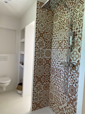 Une salle de bain avec des carreaux décorés, une douche, des toilettes et une étagère sur laquelle se trouve un panier.