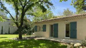 Un bâtiment d’un seul étage, doté d’un toit en tuiles, d’un petit porche et d’un jardin agrémenté d’un arbre et de plantes à fleurs.