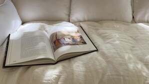 Un lit avec une literie blanche et un livre ouvert posé dessus.