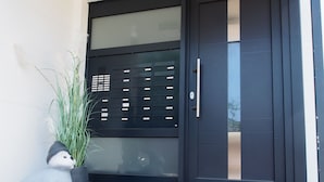 A modern building entrance with a black door, a small outdoor seating area, and a potted plant. - Modern apartment near the beach with beach chair (Grömitz)
