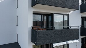 A modern building with a balcony featuring a textured black exterior, glass doors, and a small seating area with a table and chairs. - Modern apartment near the beach with beach chair (Grömitz)