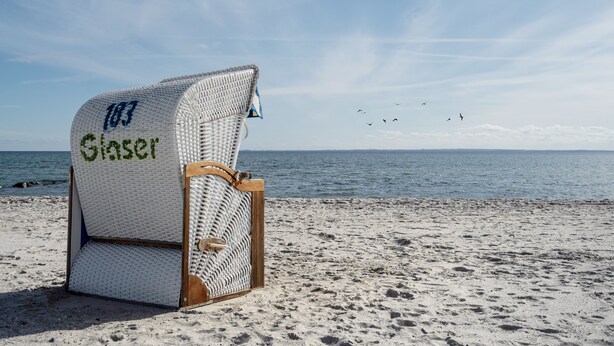 A beach chair with "Siuser" written on it, placed on a sandy beach with the ocean and birds in the background. - Modern apartment near the beach with beach chair (Grömitz)