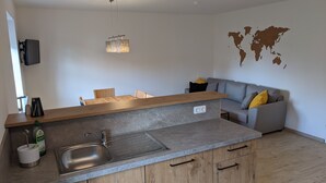 A modern kitchen with a grey countertop, wooden cabinets, and a grey sofa with yellow cushions in the living area.