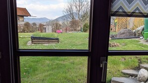 A room with a large window offering a view of a grassy yard, a wooden bench, and a stone pathway.