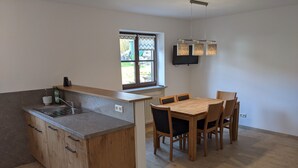 A modern kitchen with a wooden island, a dining table with chairs, a window with a view, and a flat-screen TV mounted on the wall.