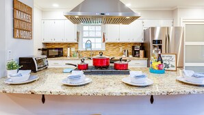 A modern kitchen with white cabinets, a stainless steel range hood, a microwave, a stove with red pots, and a refrigerator. - 3000 sq feet house- Braves, Coke, Barbie Themed Rooms next to Truist Park (Marietta)