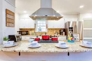 A modern kitchen with white cabinets, a stainless steel range hood, a microwave, a stove with red pots, and a refrigerator.
