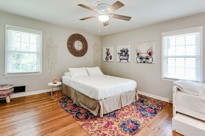 A bedroom with a bed, a ceiling fan, a round mirror, and artwork on the walls.