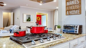 A modern kitchen with a gas stove, two red pots, a toaster, and a wall sign saying "LOVE MAKES A HOUSE A HOME". - 3000 sq feet house- Braves, Coke, Barbie Themed Rooms next to Truist Park (Marietta)