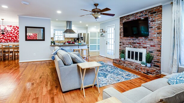 A modern living room with a fireplace, a television mounted on a brick wall, and a dining area with a red floral wall. - 3000 sq feet house- Braves, Coke, Barbie Themed Rooms next to Truist Park (Marietta)