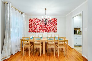 A dining area with a wooden table and chairs, a chandelier, and a floral wall decoration.