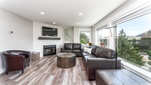 A modern living room with a fireplace, leather sofas, and a large window offering a city view. - Park Pointe A201 - Community Pool/Hot tub (Chelan)
