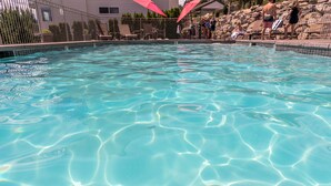 A clear swimming pool with a tiled edge, surrounded by lounge chairs and umbrellas. - Park Pointe A201 - Community Pool/Hot tub (Chelan)