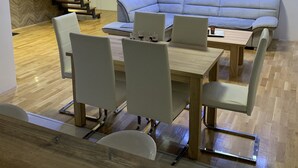Un salon moderne comprenant un canapé, une table à manger avec des chaises, un escalier et une grande fenêtre avec des stores.