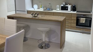 Une cuisine moderne avec des meubles en bois, un îlot central doté de tabourets, un réfrigérateur, un four à micro-ondes et une machine à café.