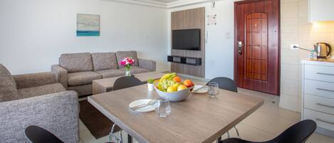 Una sala de estar moderna con un sofá, una mesa de comedor con sillas, un televisor montado en la pared y una puerta de madera.