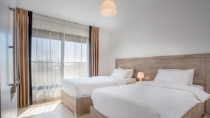 Camera d'albergo con due letti, un'ampia finestra con tende e una moderna lampada a soffitto.