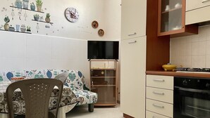 Een keuken met een eethoek, met een tafel en stoelen, een televisie, kasten en een fornuis.
