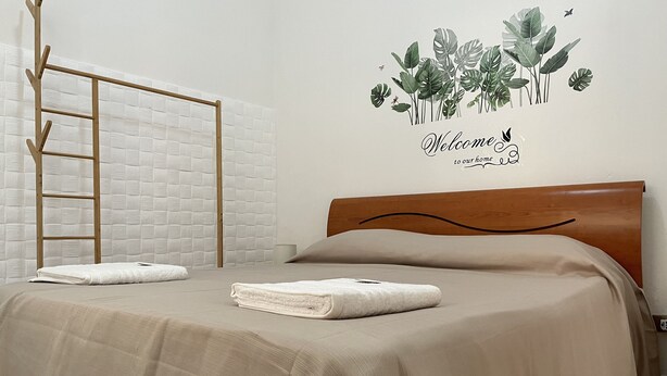 Een netjes opgemaakt bed met een houten hoofdbord, een ladder tegen de muur, en een bord met planten aan de wand.