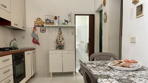 Een keuken met witte kasten, een fornuis en een eettafel met een tafelkleed met dessin.