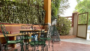 Een terras buiten met groene metalen stoelen en een tafel, omgeven door een bakstenen muur en beplanting.