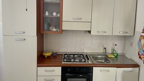 Een kleine keuken met witte kastjes, een gasfornuis, een spoelbak en een vaatwasser.