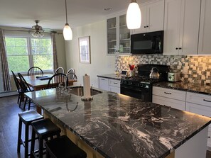 A modern kitchen with a marble island, stainless steel appliances, and a dining area with chairs and a table. - Adventurebrook, bike, ski & hike out your front door! 0.25 miles to lower lift! (East Burke)