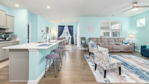 Un vaste espace de vie comprenant un grand canapé, une table à manger avec des chaises et un coin cuisine avec un bar.