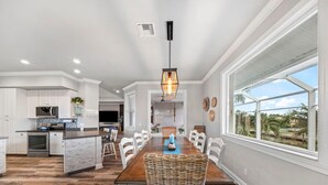 Une cuisine spacieuse dotée de meubles blancs, d’un îlot central et d’un coin repas avec une table en bois et des chaises en osier.