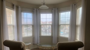 A corner room with two armchairs, a small round table, and a view of a residential area through large windows with blinds. - Stunning entire house in Channel Islands Marina (Oxnard)