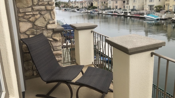 A balcony with a stone wall, a chair, and a view of a marina with boats and houses. - Stunning entire house in Channel Islands Marina (Oxnard)
