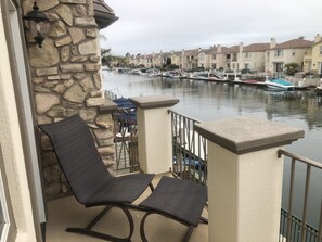 A balcony with a stone wall, a chair, and a view of a marina with boats and houses. - Stunning entire house in Channel Islands Marina (Oxnard)