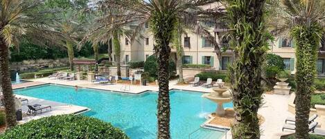 A swimming pool surrounded by palm trees and lounge chairs, with a building in the background.