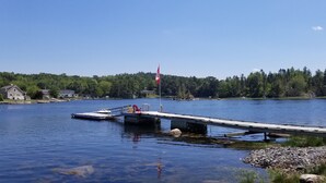 A dock extending into a lake with a flag, a boat, and a house in the background.
