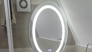 Une salle de bain avec un lavabo blanc, un miroir avec un éclairage intégré et un porte-serviettes.