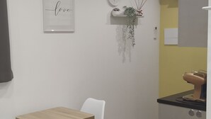 Une cuisine moderne avec des armoires blanches, une table en bois et deux chaises blanches. Un tableau encadré est accroché au mur et une petite plante est posée sur une étagère.