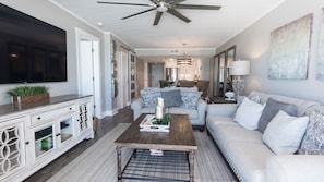 A spacious living room with a large flat-screen TV, a ceiling fan, and a cozy seating area with a sofa and coffee table. - 5 STAR BEACHFRONT 2BR/2BA • Dunes of Panama D505 • Nov & Dec Snowbird Available! (Panama City Beach)