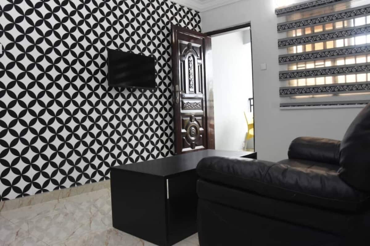 A modern room with a geometric patterned wall, a black leather sofa, and a wooden door with intricate designs.
